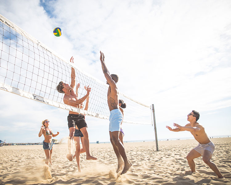 Sechs junge Menschen spielen Beachvolleyball am sonnigen Nordseestrand