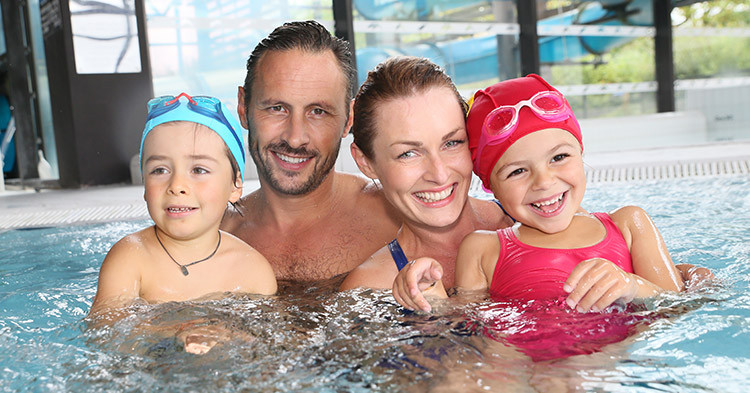 Lächelnde Eltern mit Tochter und Sohn stehen bis zu den Schultern im Wasser eines Schwimmbeckens