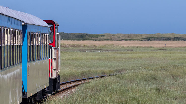 Teilansicht der Inselbahn auf Wangerooge, die durch grüne Salzwiesen in Richtung Küste fährt