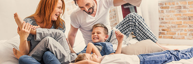 Lachende Eltern mit Tochter und Sohn beim Spielen im Bett eines Hotelzimmers