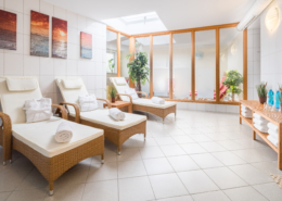 Heller, weiß gefliester Ruheraum mit gepolsterten Rattanliegen im Wellnessbereich des Hotels auf Wangerooge