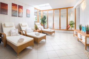 Heller, weiß gefliester Ruheraum mit gepolsterten Rattanliegen im Wellnessbereich des Hotels auf Wangerooge