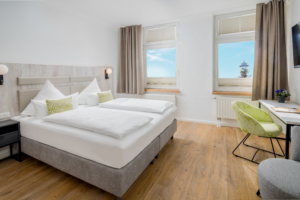 Helles Schlafzimmer einer Suite im Parkhotel Wangerooge mit großem gemachtem Doppelbett, Sessel, Schreibtisch und Leuchtturmblick