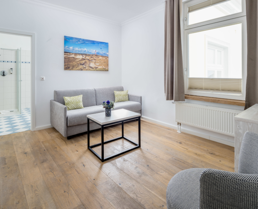 Wohnbereich einer Suite im Parkhotel Wangerooge mit Sofa, Couchtisch, großem Fenster und Blick ins Badezimmer