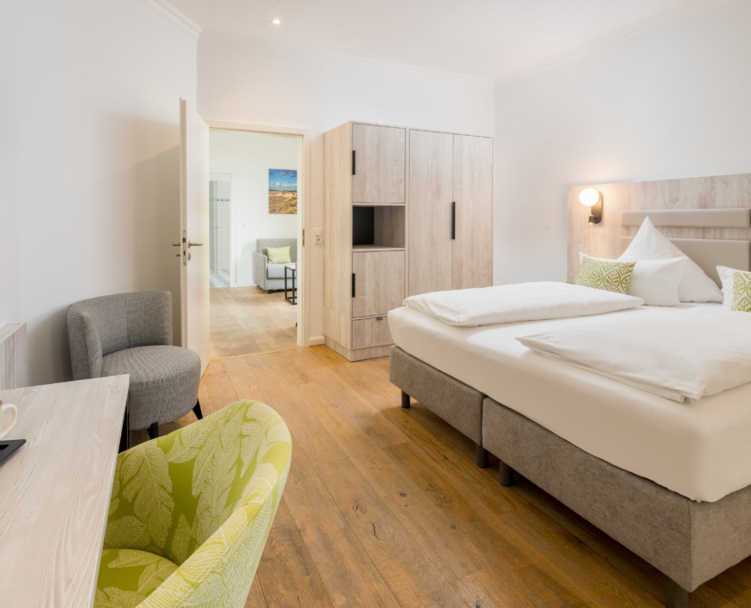 Schlafzimmer einer Suite im Parkhotel Wangerooge mit Doppelbett, Schreibtisch, großzügigem Stauraum und Blick in den angrenzenden Wohnbereich