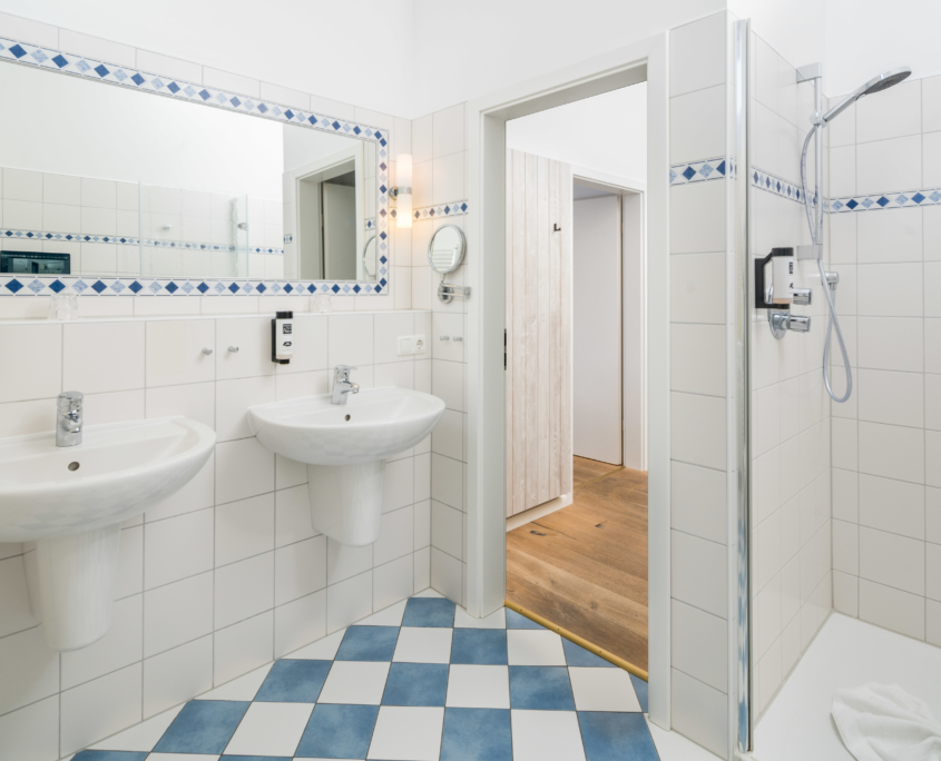 Badezimmer im Parkhotel Wangerooge mit zwei Waschbecken, großer Dusche und dekorativen Elementen aus blau-weißen Fliesen