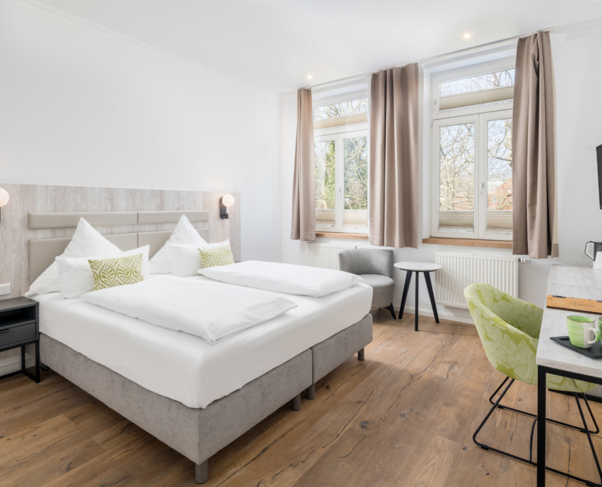 Helles Doppelzimmer im Parkhotel Wangerooge mit großem, gemachtem Bett, Schreibtisch, Sitzbereich und Blick ins Grüne