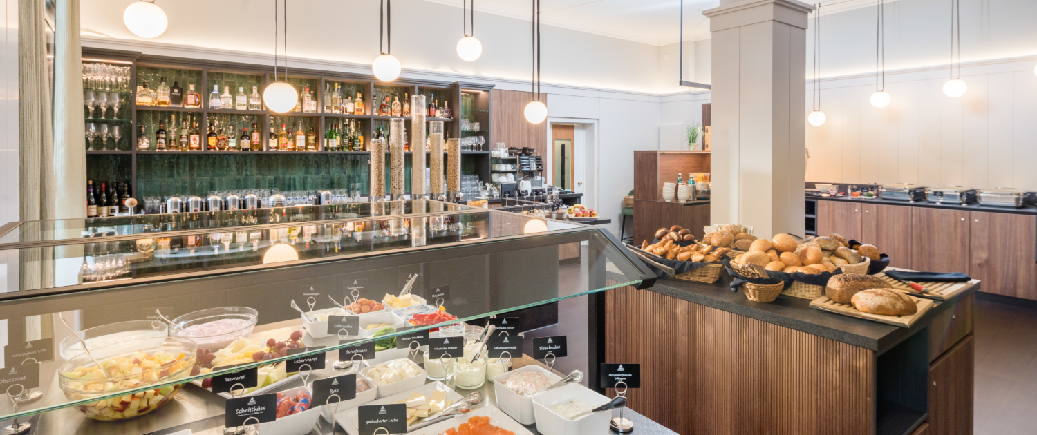 Gesamtansicht der verschiedenen Frühstückstresen im Parkhotel Wangerooge, unter anderem mit Aufschnittvariationen, Lachs, Joghurt, Obst und Gemüse, frischen Brötchen, Eierspeisen, Aufstrichen, Müsli und Getränkeauswahl