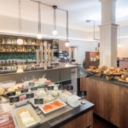 Gesamtansicht der verschiedenen Frühstückstresen im Parkhotel Wangerooge, unter anderem mit Aufschnittvariationen, Lachs, Joghurt, Obst und Gemüse, frischen Brötchen, Eierspeisen, Aufstrichen, Müsli und Getränkeauswahl
