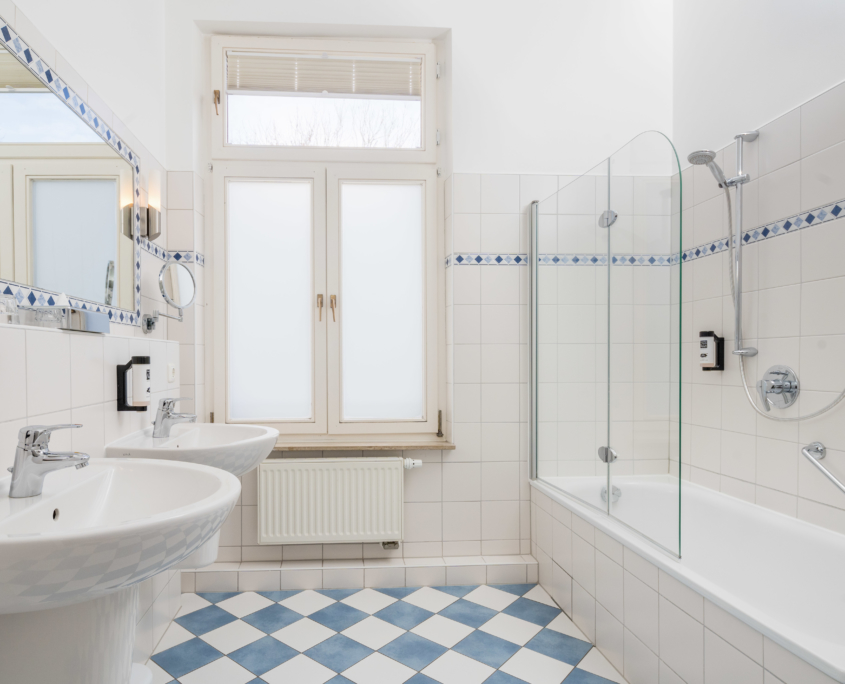 Blau-weiß gefliestes Tageslichtbad im Parkhotel Wangerooge mit zwei Waschbecken, Badewanne mit Dusche und großem Spiegel