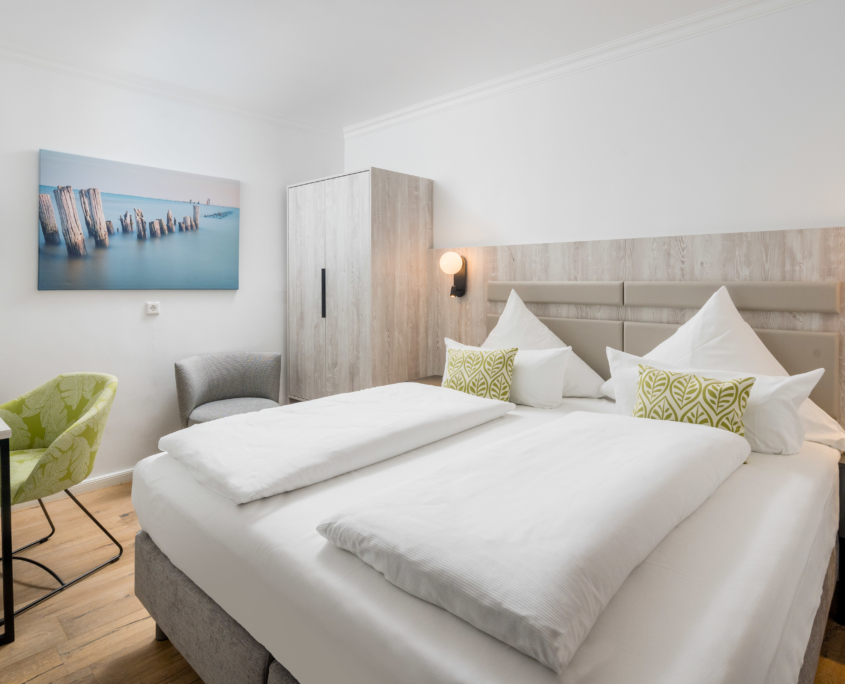 Modernes Doppelzimmer im Parkhotel Wangerooge mit gemachtem Bett, Schreibtisch, Sessel und maritimer Wanddekoration