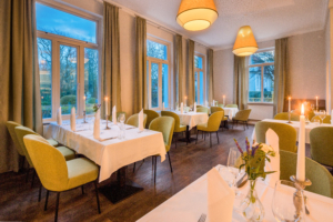 Restaurantbereich im Parkhotel Wangerooge zur Abendzeit mit eingedeckten Tischen, weißen Tischdecken, Kerzen und Blumen