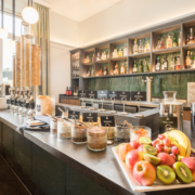 Frühstückstresen im Parkhotel Wangerooge mit vielfältiger Müsliauswahl, frischem Obst, Nüssen, Kernen, Trockenfrüchten und Milch vor einem modernen Barregal