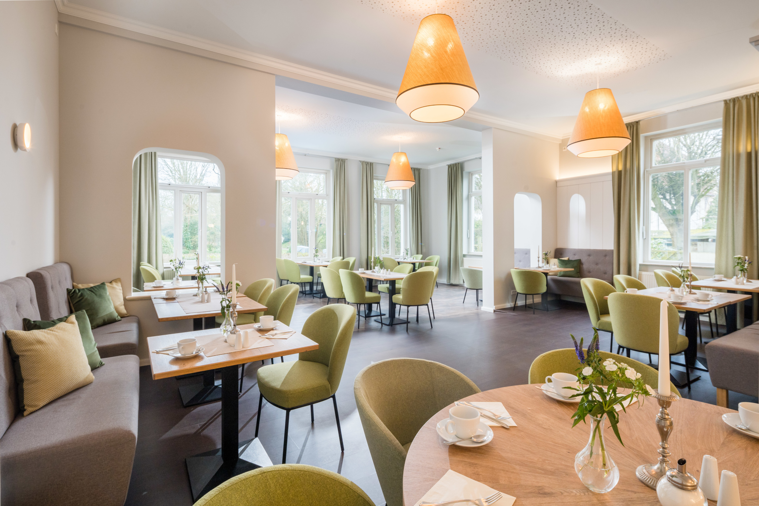 Heller, modern eingerichteter Restaurantbereich im Parkhotel Wangerooge mit grünen Stühlen, Sitzbänken mit Kissen, eingedeckten Tischen und großen Fenstern
