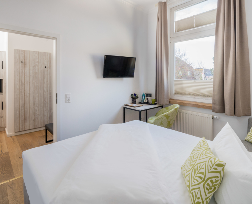 Einzelzimmer im Parkhotel Wangerooge mit Schreibtisch, Flachbild-TV, gemachtem Bett, Eingangsbereich mit Stauraum und Blick auf den Ort