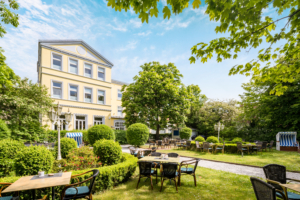 Sonniger Gartenbereich des Parkhotel Wangerooge mit gemütlichen Sitzplätzen, Strandkörben und Blick auf das historische Haupthaus
